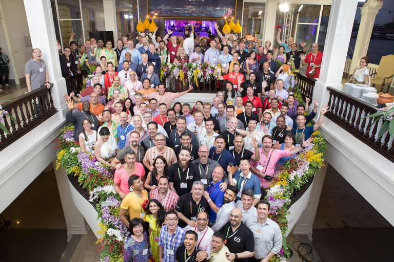 A large group of successful entrepreneurs poses on a beautiful stairwell.
