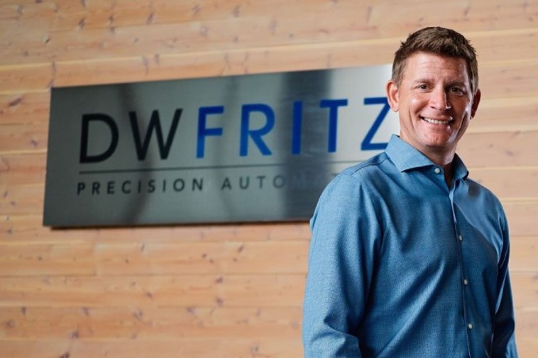 A successful man stands in front of a sign reading DW Fritz.