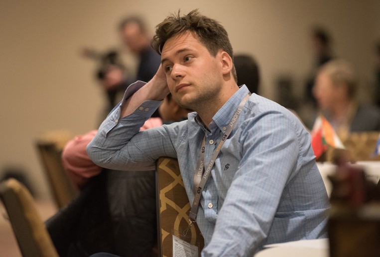 A worried man in business casual attire rests his head on his hand.