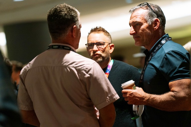 Three men in casual business attire have an intense discussion over coffee.