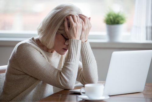 Frustrated employer holds head in hands at desk.