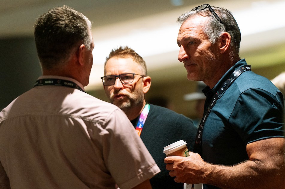 Three men in casual clothes have an intense conversation.