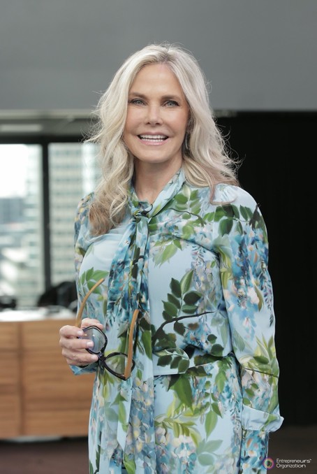 A woman in a floral dress stands ready to make a presentation with her glasses in hand.