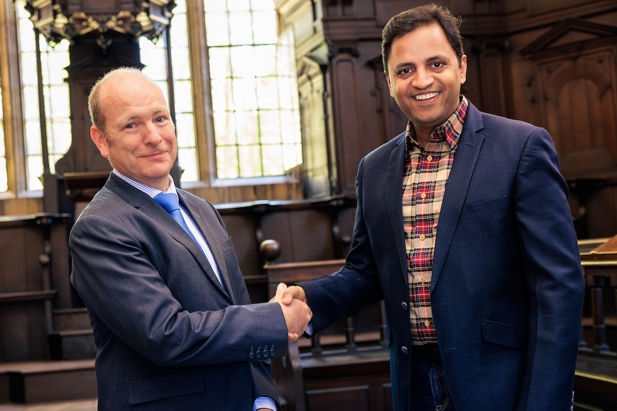 Two men in suits shake hands with a smile.