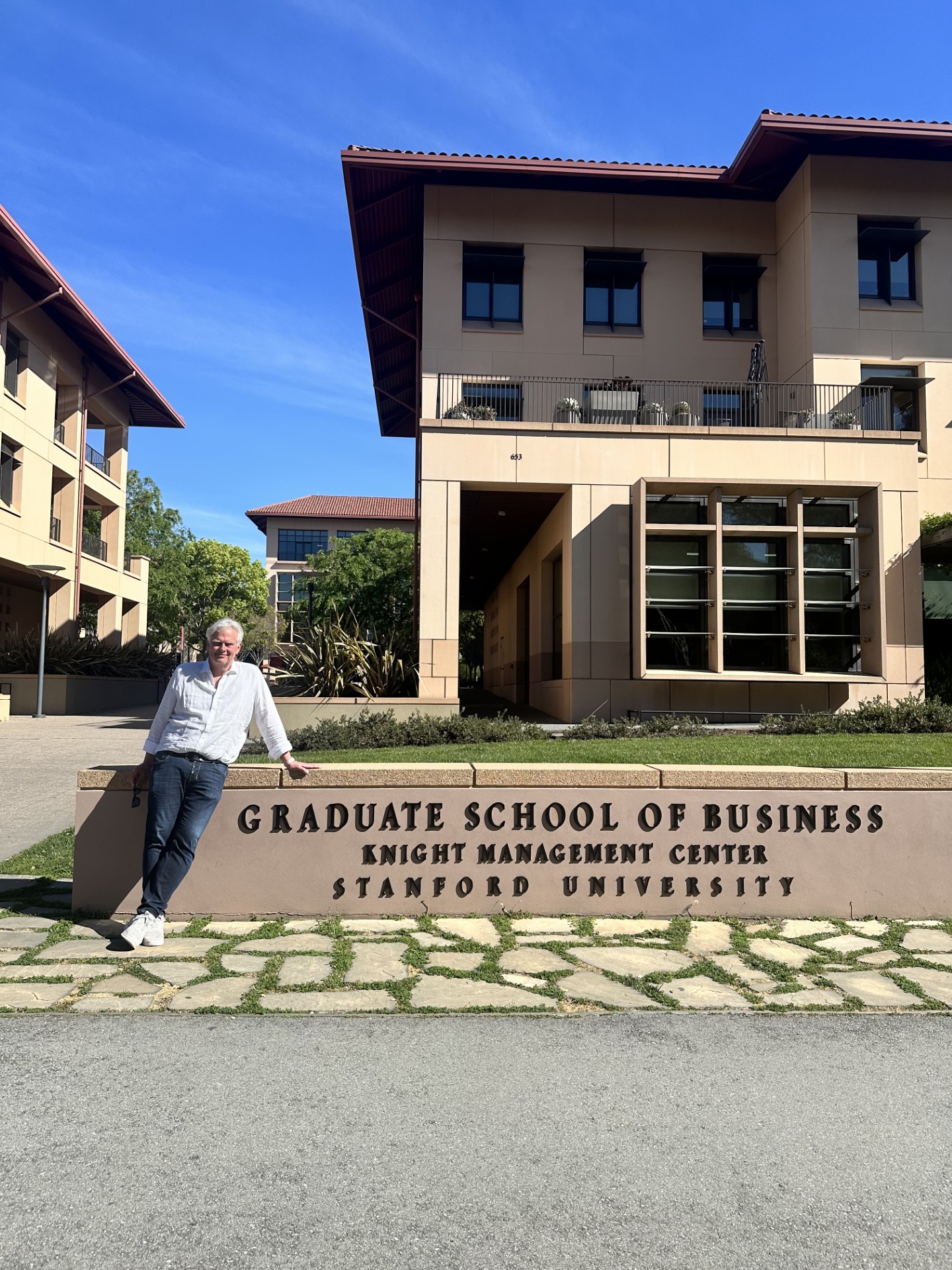 A man poses in front of the sign at Stanford University Graduate School of Business