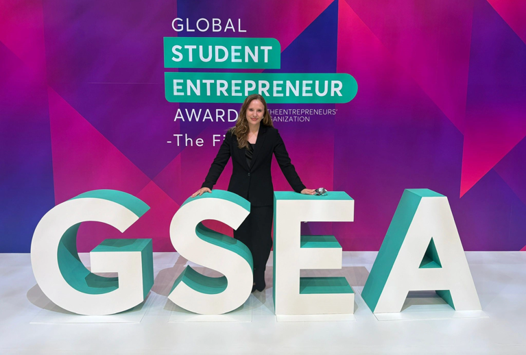 A woman in a black suit stands in front of EO's GSEA signage.