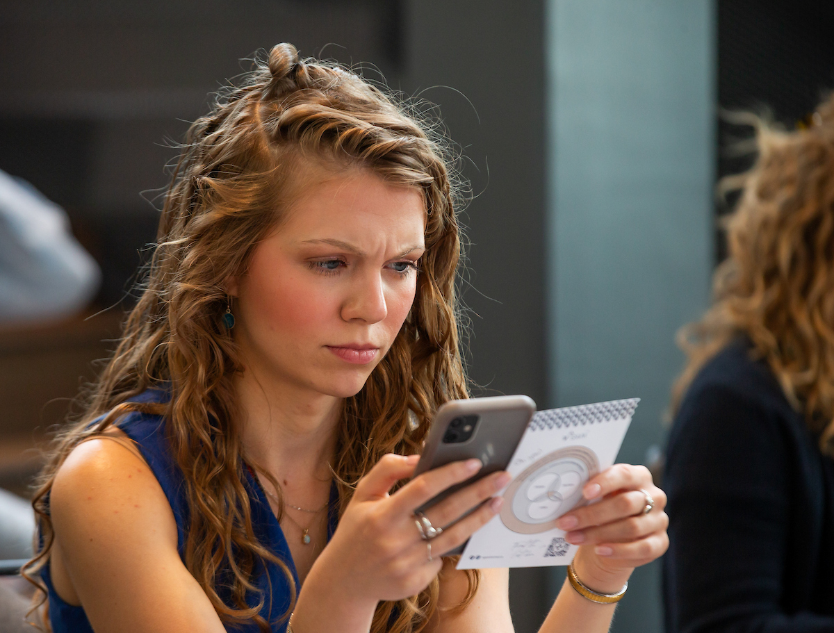 A young woman studies her phone with a look of deep thought on her face.