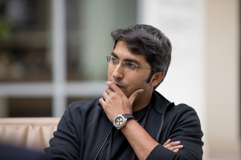 A man dressed in business casual attire rests a hand on his face in a contemplative posture.