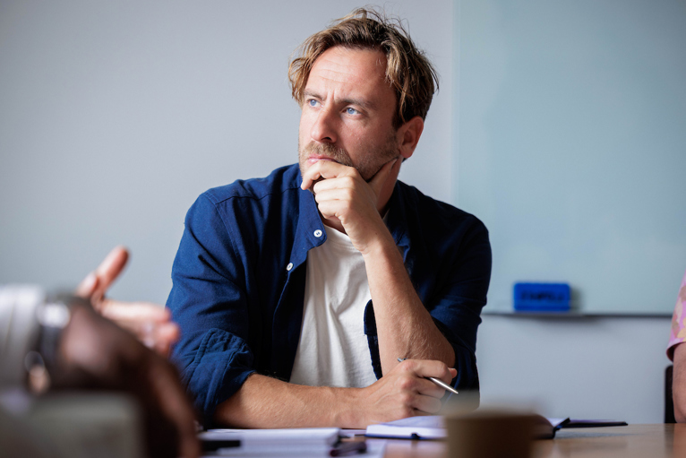 A man sits at a desk with chin in hand, appearing to be in deep thought.