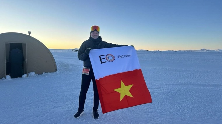 A man displaying an EO Vietnam flag stands on the frozen tundra of Antarctica.