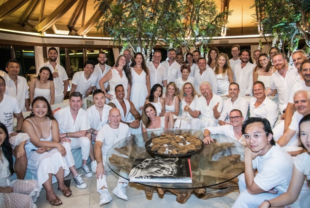 A large group of MyEO members gather for a photo on Necker Island, all dressed in white.