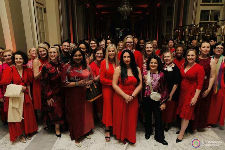 Dozens of entrepreneurial women stand together in red dresses.