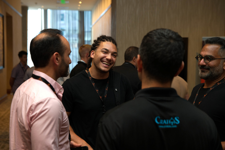 Four men stand in a circle together talking, the youngest with a big smile.