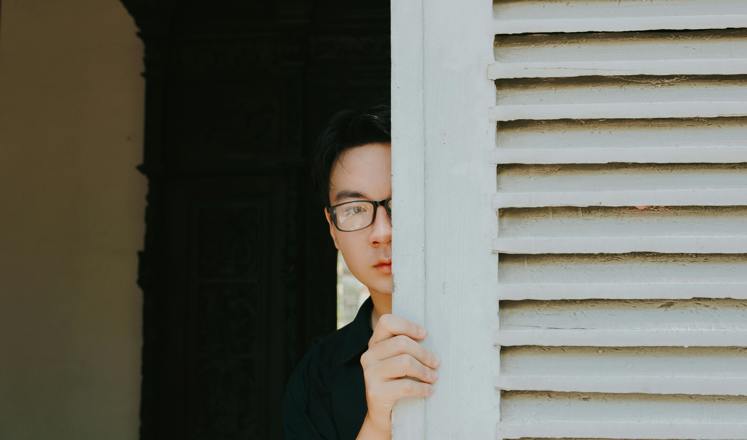 Asian man in glasses peeks around door