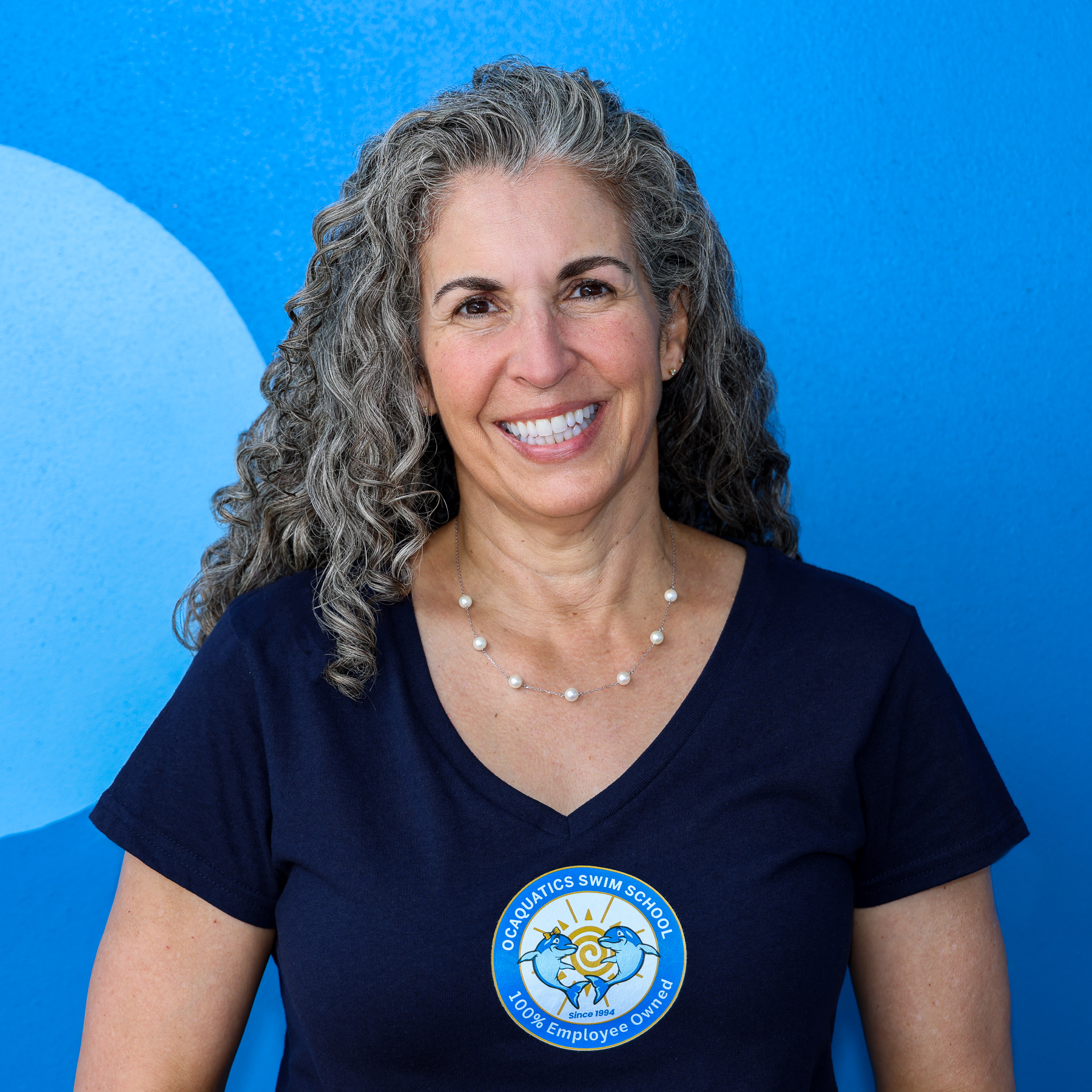 A woman with gray curly hair dressed in a branded Ocaquatics shirt.