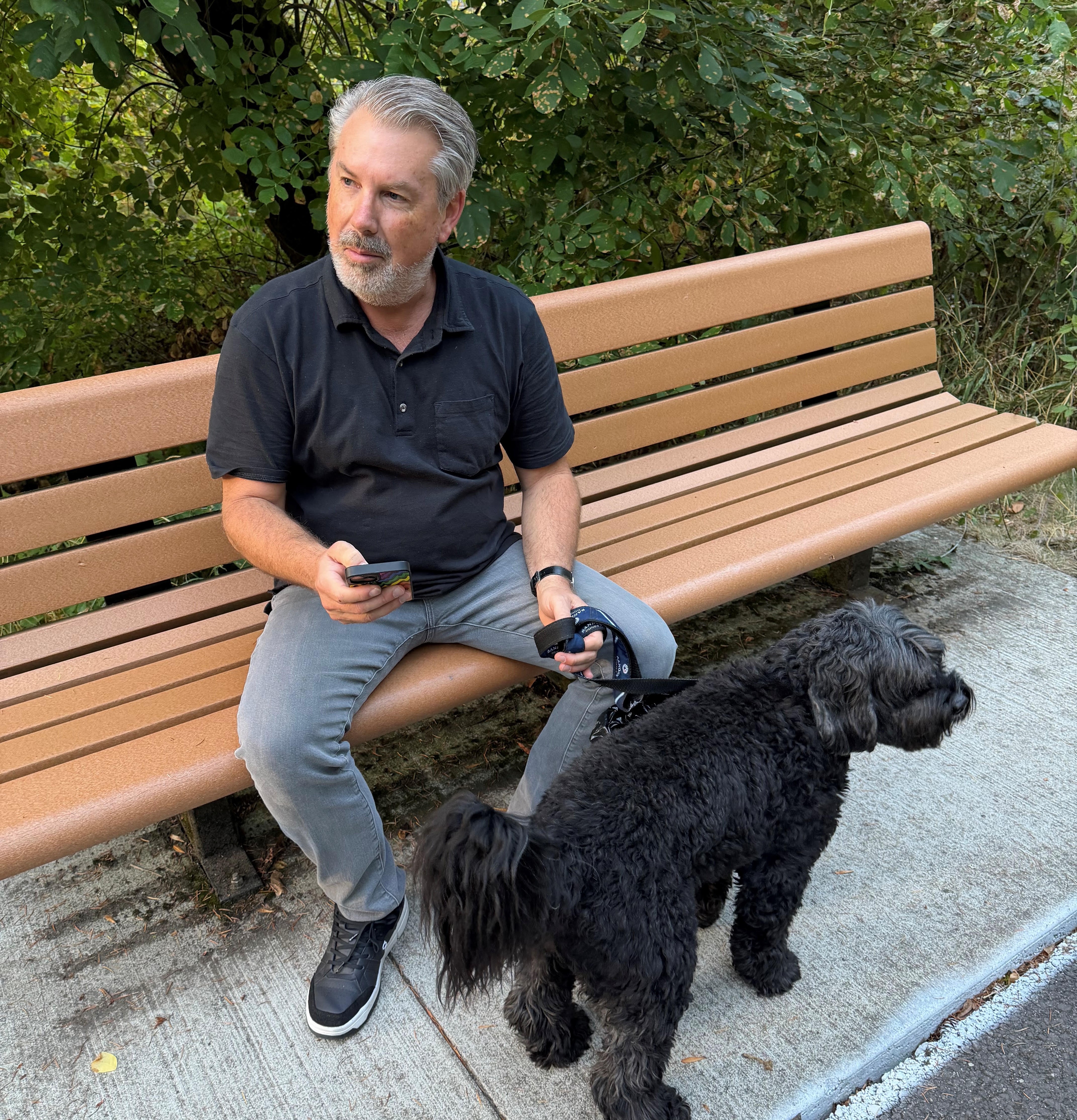 Barry Raber sits on a park bench with his cell phone and dog.