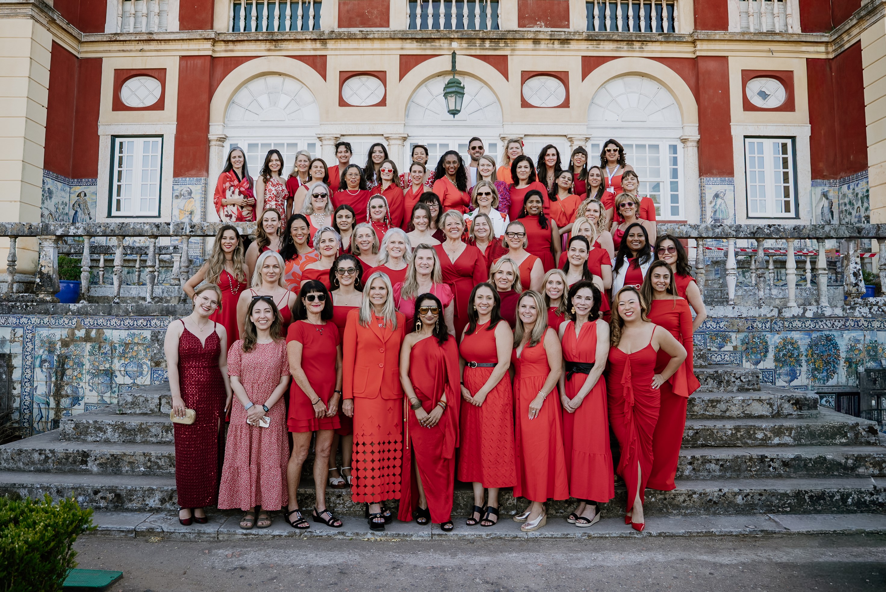 Dozens of women in red dresses pose in a beautiful setting.