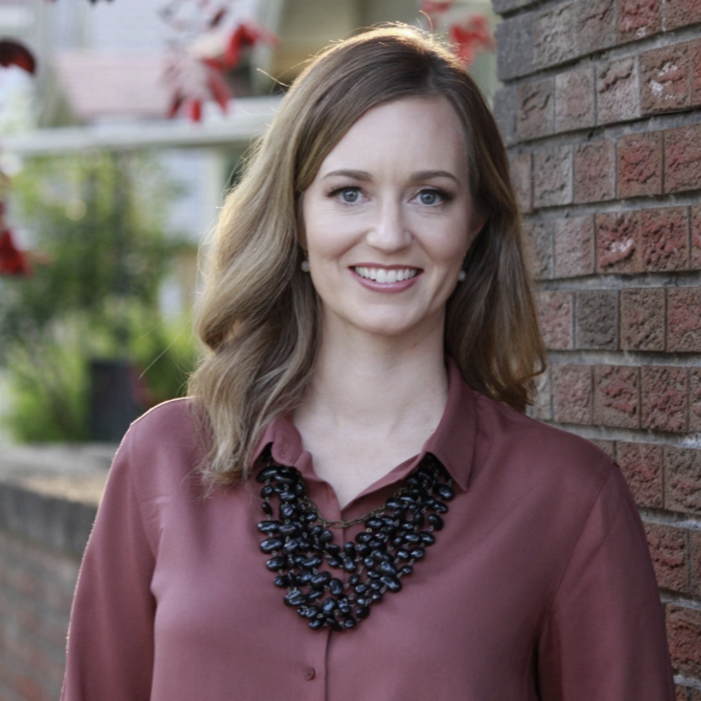 Close-up image of a woman in business attire smiling in an urban setting.