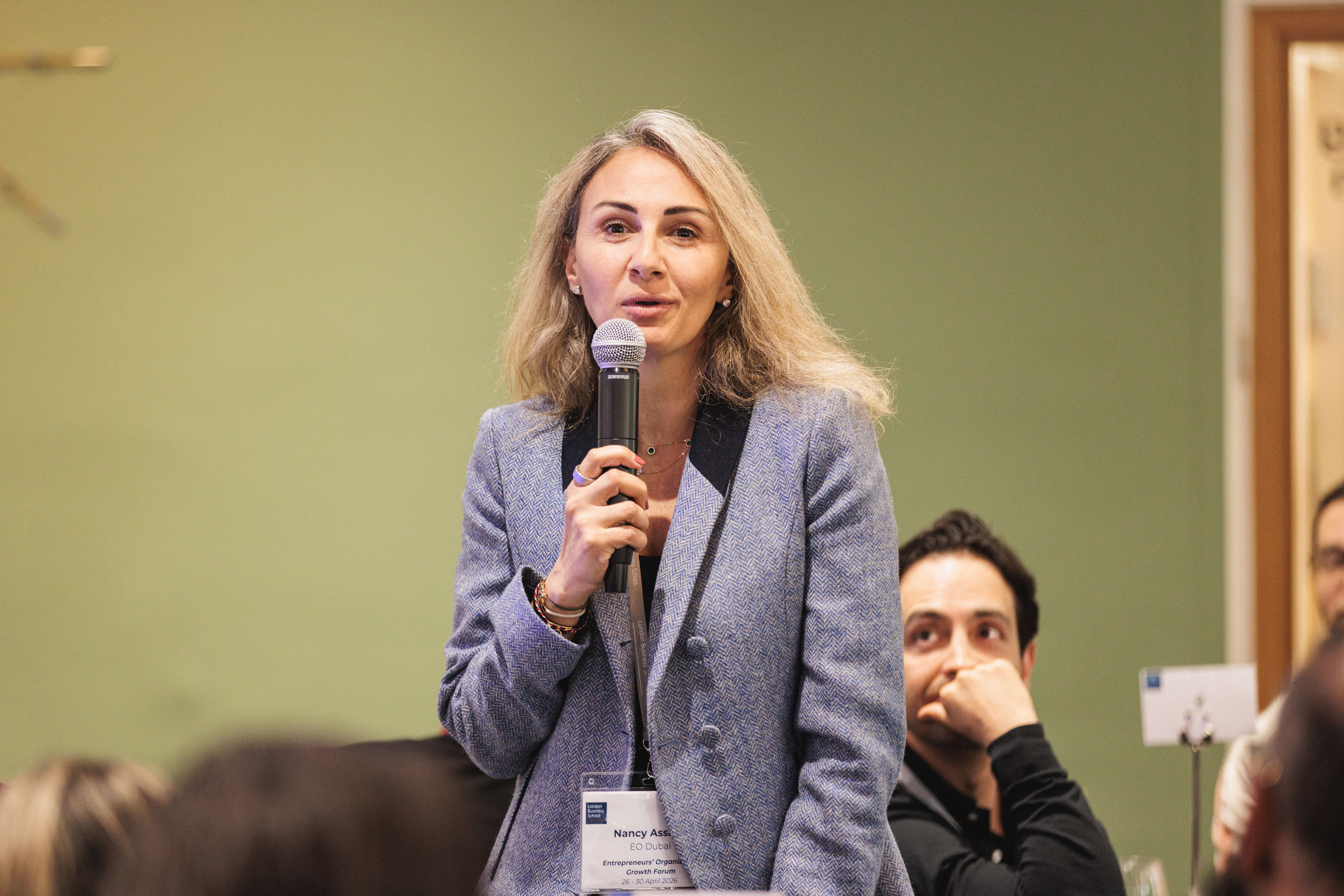 A woman in business attire speaks confidently into a microphone.