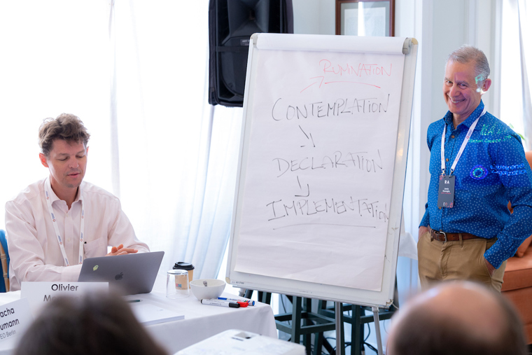 A businessman presents  ideas on a whiteboard while others take notes.
