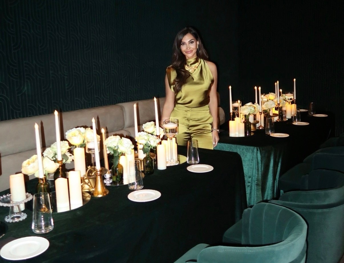 A confident woman in evening attire stands near a beautifully set table.