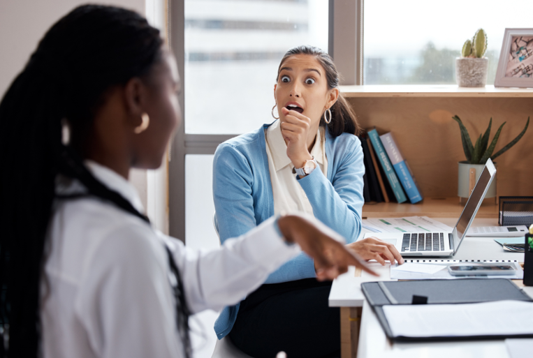 Two women in an office setting show body language signs of being in conflict.