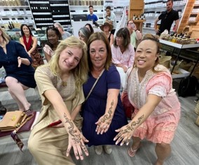 Three seated women extend their arms to show henna tattoos.