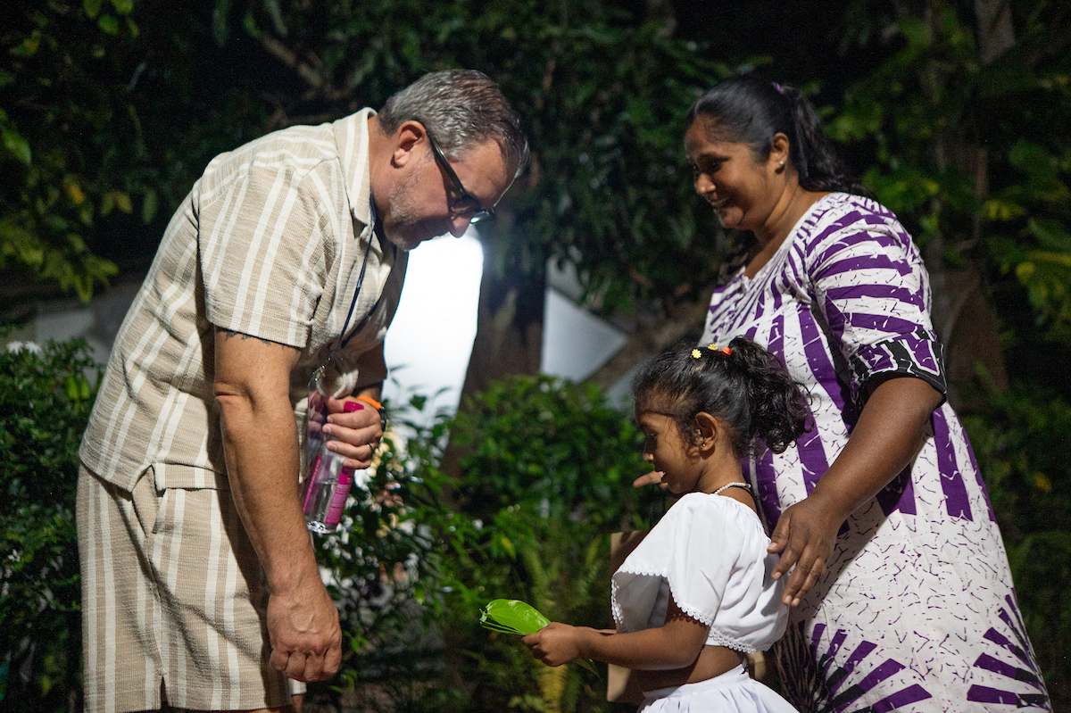 A father leans down to hear his young daughter as her mother stands close.