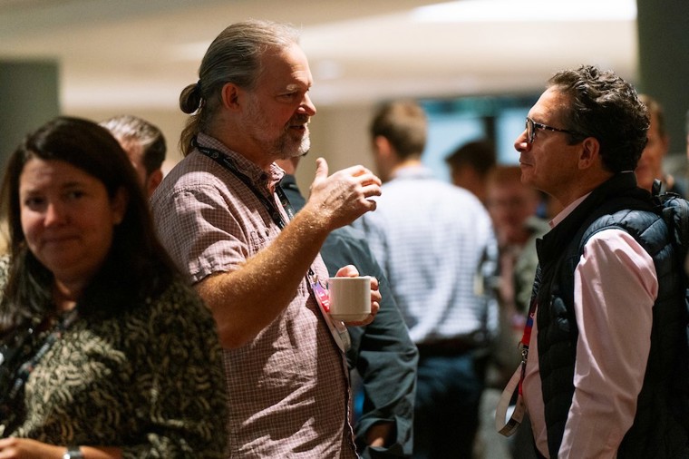 Two business men talk passionately in a room full of entrepreneurs.