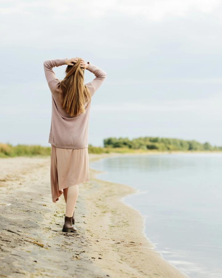 Blonde woman walking on lakeshore holding the back of her head