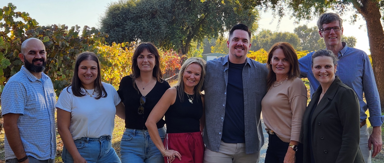 Eight members of the Merlot Marketing team pose in an outdoor setting.